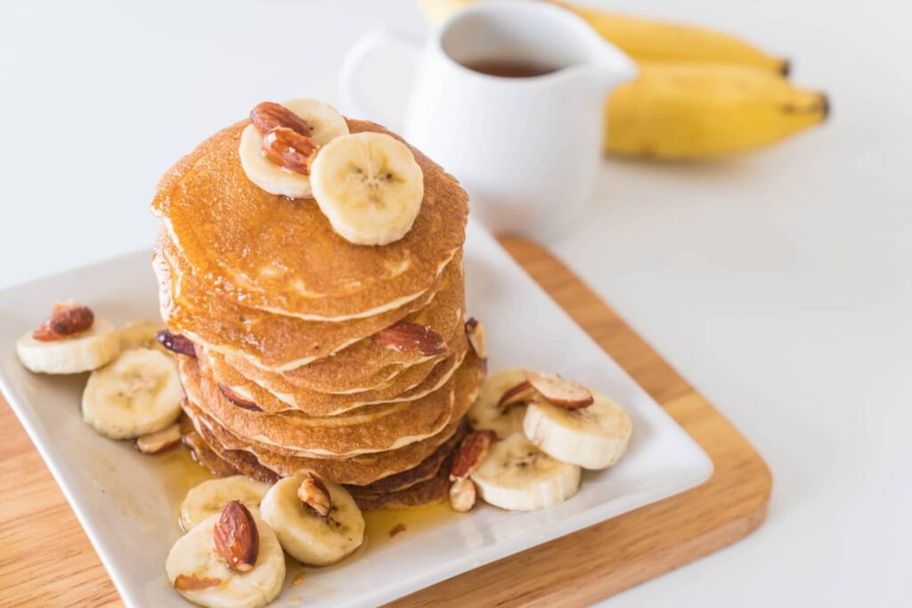 Plato de tortitas con rodajas de platano y chocolate caliente.